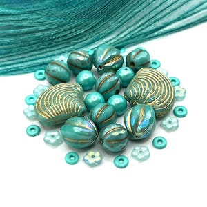 May include: A collection of turquoise beads in various shapes, including two large shell-shaped beads with gold-colored grooves, round faceted beads with gold accents, smooth round beads, and small flower-shaped beads scattered throughout.
