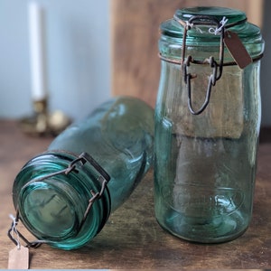 Puede incluir: Dos tarros de vidrio verde vintage con tapas de metal y cierres de alambre. Los tarros están vacíos y tienen un aspecto rústico.