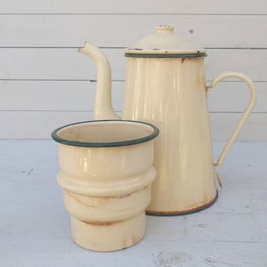 Könnte beinhalten: Eine vintage Kaffeekanne aus cremefarbenem Emaille mit grünem Rand und eine passende Tasse aus cremefarbenem Emaille mit grünem Rand.