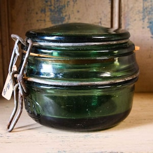 Può includere: Un barattolo di vetro verde vintage con un coperchio di metallo e una chiusura di metallo. Il barattolo ha un'etichetta che dice "B192".