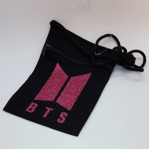 May include: Black drawstring bag with a pink glitter BTS logo and the text "BTS".