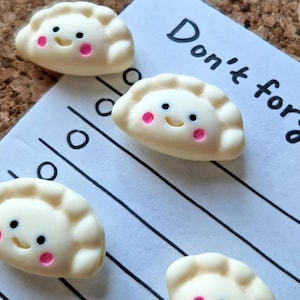 May include: Four white dumplings with pink cheeks and black eyes, smiling. The dumplings are arranged on a white sheet of paper with black lines. The text "Don't forget" is written in black ink on the paper.