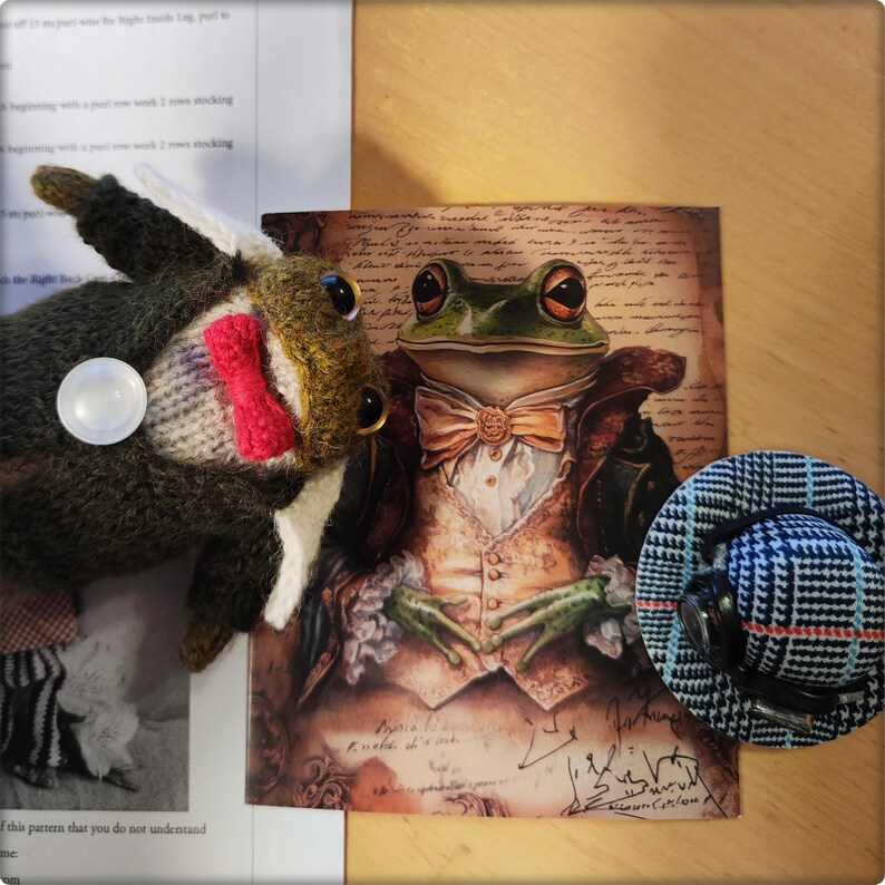 May include: An artistic composition featuring a frog illustration in formal attire, a knitted frog toy with a bow tie, and a small plaid hat. The frog illustration has a bow tie and a vest. The knitted frog toy has a red bow tie.