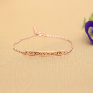 May include: A rose gold bracelet with a thin bar charm engraved with the coordinates "40°57.93'N 5°38.93'W".