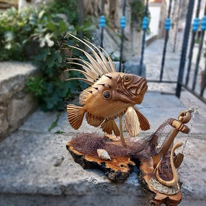 K&ouml;nnte beinhalten: Eine Holzskulptur eines Fisches mit einer stacheligen Flosse, einem Anker und einem Netz auf einem Holzsockel.