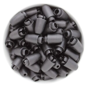 May include: A collection of black plastic cord locks, cone-shaped with a slotted opening at the base. The cord locks are tightly packed together, filling the frame against a white background. These small components are used for securing cords.