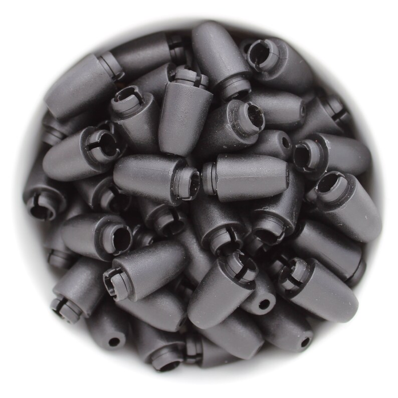 May include: A collection of black plastic cord locks, cone-shaped with a slotted opening at the base. The cord locks are tightly packed together, filling the frame against a white background. These small components are used for securing cords.