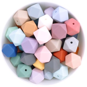 May include: A bowl filled with a variety of colorful silicone teething beads. The beads are shaped like geometric diamonds and have a hole in the center. The beads are in shades of blue, green, pink, purple, brown, gray, and orange.