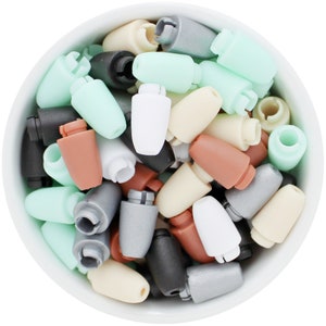 May include: A white bowl filled with a variety of colorful, small, plastic objects. The objects are in shades of white, black, gray, brown, and mint green. The objects have a unique shape with a cylindrical body and a notched top.