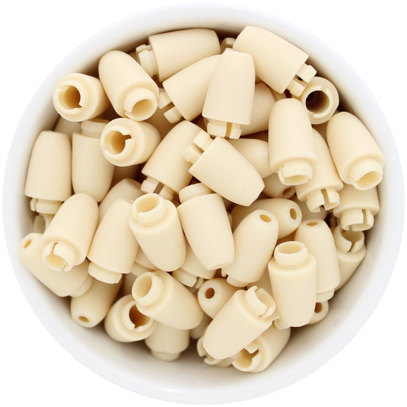 May include: A white bowl filled with numerous small, off-white plastic components. Each component has a cylindrical base and a tapered, rounded top. The components are densely packed, filling the bowl and creating a uniform texture.