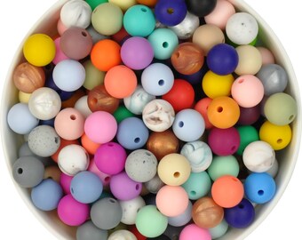 May include: A bowl filled with colorful silicone beads. The beads are various shades of blue, green, pink, red, yellow, orange, brown, and gray. Some beads have a marbled or speckled pattern.