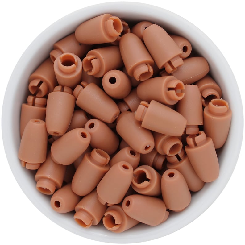 May include: A collection of small, light brown plastic earbud tips, filling a white bowl. The tips have a rounded, conical shape with a small opening at the top and a notched base. The overall impression is of a bulk supply of replacement earpieces.