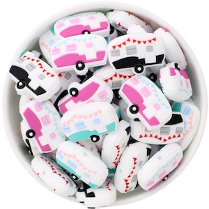 May include: A bowl filled with white, pink, and blue campervan-shaped beads. Each bead has a detailed design with windows, wheels, and bunting. The beads are made of a smooth material, perfect for crafting. The beads are approximately 2 cm in length.