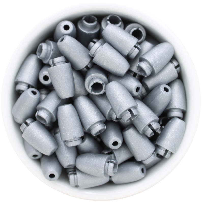 May include: A collection of silver-colored, bullet-shaped fishing weights, each with a slotted end and a small hole at the top. The weights are contained within a white bowl, creating a contrast with their metallic sheen.