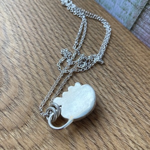 May include: A silver chain necklace with a silver pendant shaped like a heart. The pendant has a smooth, brushed finish.