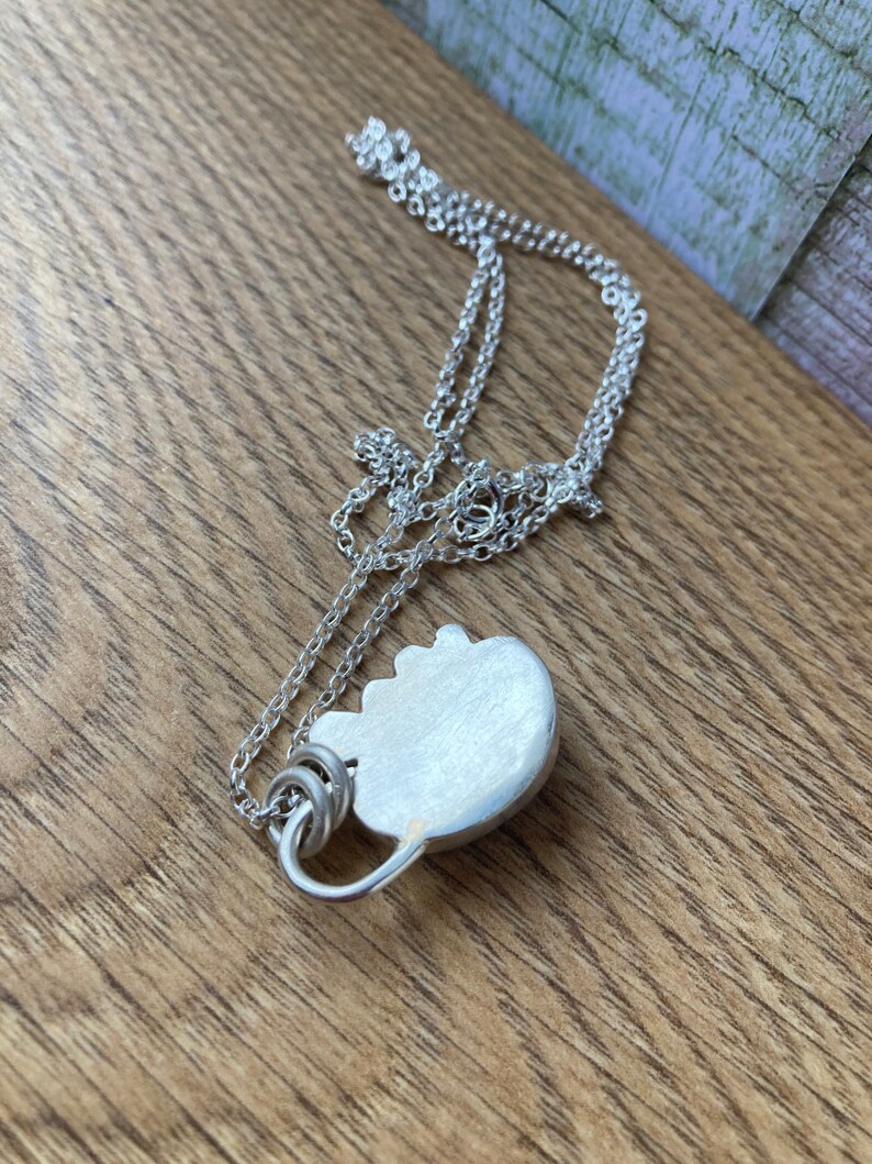May include: A silver chain necklace with a silver pendant shaped like a heart. The pendant has a smooth, brushed finish.