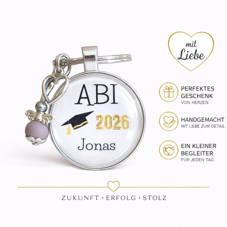 Pu&ograve; includere: Un portachiavi argentato con un ciondolo rotondo con la scritta "ABI 2026 Jonas" e una grafica di cappello di laurea. Il portachiavi include un ciondolo decorativo con un cuore e una perla lavanda. L'immagine include anche testo in tedesco.