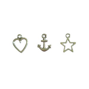 May include: Three silver-colored charms: a heart, an anchor, and a star. Each charm has a small loop at the top for attaching to a necklace or bracelet. The heart and star are open designs, while the anchor is solid.