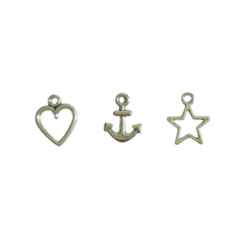 May include: Three silver-colored charms: a heart, an anchor, and a star. Each charm has a small loop at the top for attaching to a necklace or bracelet. The heart and star are open designs, while the anchor is solid.