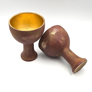 Può includere: Due calici rossi e dorati con una finitura usurata. I calici sono in ceramica e hanno una ciotola larga e rotonda e uno stelo alto e sottile.