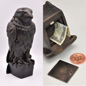 May include: A dark bronze-coloured falcon figurine with a hollow interior designed as a coin bank. The sculpture features a removable square base plate and is shown with a one-dollar bill inserted into the slot and a copper-coloured bitcoin token.