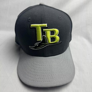 May include: A gray and black baseball cap with a yellow and black embroidered Tampa Bay Rays logo. The logo features the team's initials "TB" and a stylized stingray.