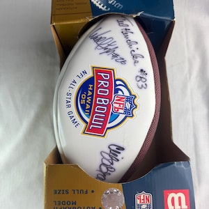 Peut inclure: Un ballon de football NFL Pro Bowl dans une boîte. Le ballon blanc a des coutures marron et plusieurs signatures. La boîte est marron et bleue avec les mots "AUTOGRAPH MODEL FOOTBALL FULL SIZE" imprimés dessus. Le ballon a un autocollant "NFL PRO BOWL HAWAII '05".