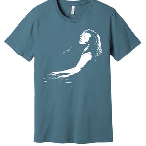 May include: A teal blue t-shirt with a white silhouette of a person playing a keyboard.
