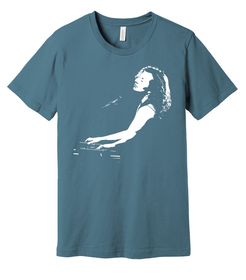 May include: A teal blue t-shirt with a white silhouette of a person playing a keyboard.