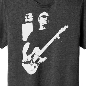 Puede incluir: Una silueta blanca de una persona tocando una guitarra eléctrica. La persona lleva gafas de sol y tiene el pelo corto. La guitarra es una Fender Stratocaster.