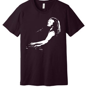 May include: A maroon t-shirt with a white silhouette of a person playing a keyboard.