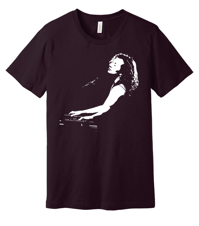 May include: A maroon t-shirt with a white silhouette of a person playing a keyboard.