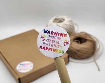 May include: A white sticker with a rainbow design and the text "WARNING OPENING THIS PACKAGE WILL RESULT IN EXTREME HAPPINESS" on a brown cardboard box.