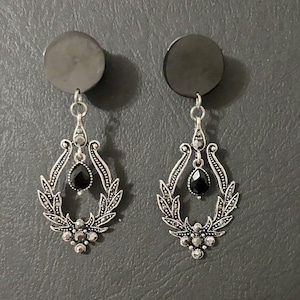 May include: A pair of silver dangle earrings with black gemstone accents. The earrings feature a teardrop-shaped stone surrounded by a decorative silver frame.