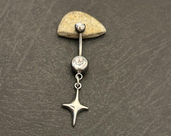 May include: A silver belly button ring with a star charm. The ring features a curved barbell with a small, clear gem at the top and a larger, clear gem at the bottom. A four-pointed star hangs from the bottom gem.