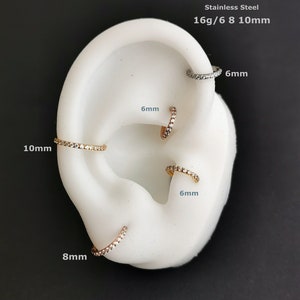 May include: Stainless steel clicker earrings with a row of clear cubic zirconia stones. The earrings are available in 6mm, 8mm, and 10mm sizes.