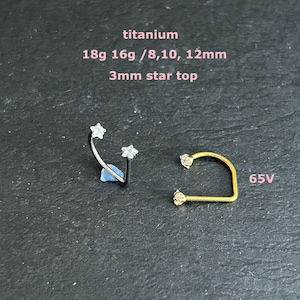 May include: Two pieces of body jewellery on a dark surface. One is a curved barbell with star-shaped ends. The other is a gold-coloured, U-shaped piece with star-shaped ends. Text reads: titanium, 18g 16g /8,10, 12mm, 3mm star top, and 65V.