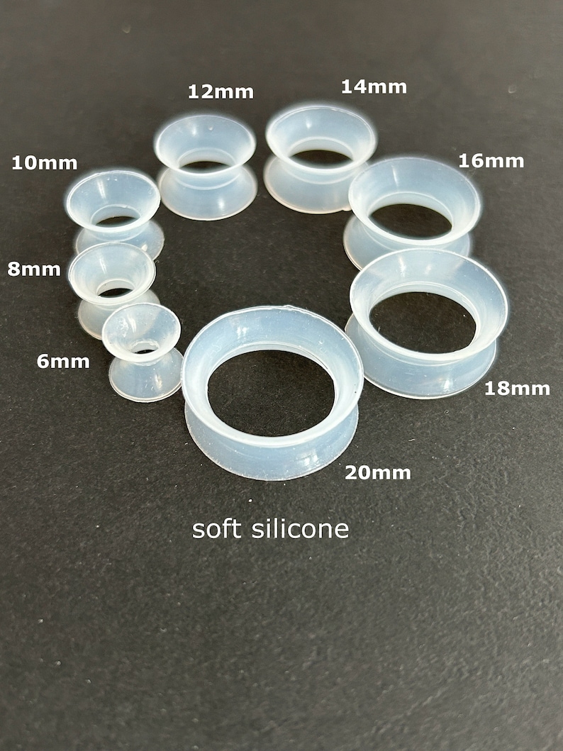 May include: A collection of clear, soft silicone ear gauges in various sizes, ranging from 6mm to 20mm. Each gauge is labeled with its size in millimeters. The text "soft silicone" is also present.