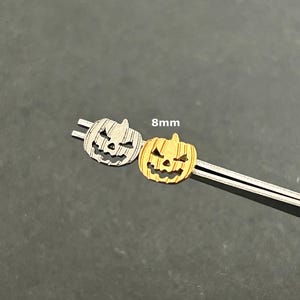 May include: Two 8mm pumpkin charms, one silver and one gold, with a carved jack-o'-lantern face.