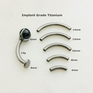 Könnte beinhalten: Ein Satz von fünf Titan-Körper-Schmuckringen in verschiedenen Größen von 6 mm bis 14 mm. Die Ringe sind aus implantatfähigem Titan gefertigt und in 14 Gauge erhältlich. Das Bild zeigt auch eine Nahaufnahme eines 5 mm Titanrings mit einem schwarzen Edelstein.