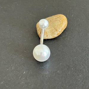 May include: A silver belly button ring with two white pearl-like beads.