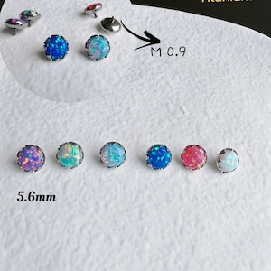May include: An assortment of G23 titanium body jewelry with opal-like gemstones. The jewelry is available in various colors, including blue, pink, and white. The gemstones are 5.6mm in diameter. The image also includes the text "M 0.9".