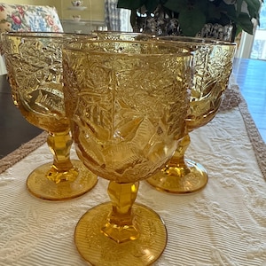 May include: Three amber glass goblets with a floral pattern. The goblets have a wide bowl and a tall stem.