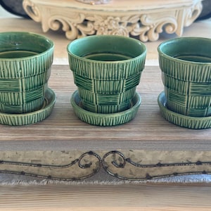 May include: Three matching green ceramic plant pots with integrated saucers. Each pot features a textured, basket-weave pattern with vertical lines on the exterior surface. The pots have a tapered, cylindrical shape and a glossy finish.