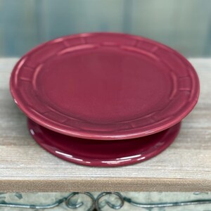 May include: A deep red ceramic cake stand with a raised rim and a smooth, glossy finish.