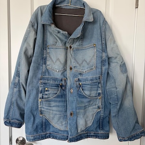 May include: A light blue denim jacket featuring a dark gray fleece lining, a classic collar, and a front button closure. The garment includes two chest pockets with a stitched W design and two lower pockets with metallic rivets and visible seams.