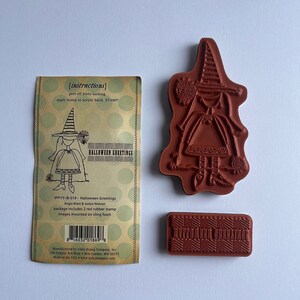 May include: A set of Halloween-themed rubber stamps. The set includes a witch stamp, a patterned stamp, and a package with instructions and the text "Halloween Greetings". The stamps are red and the package is tan with green polka dots.