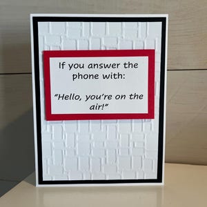 May include: A greeting card with a white textured background and a black border. A red rectangle in the center contains the text: "If you answer the phone with: 'Hello, you're on the air!'"
