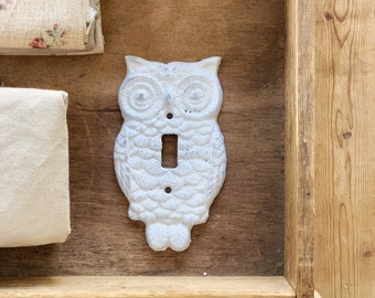 May include: White ceramic owl light switch cover. The owl has a detailed design with feathers and large eyes. The switch cover is mounted on a wooden surface.