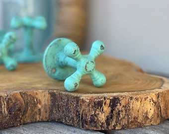 Op de afbeelding: Een set van drie turquoise blauwe metalen haken in de vorm van vintage waterkranen. De haken zijn gemonteerd op een houten schijf.